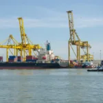 Kapal kargo bersandar di pelabuhan dengan crane dan kontainer ekspor impor